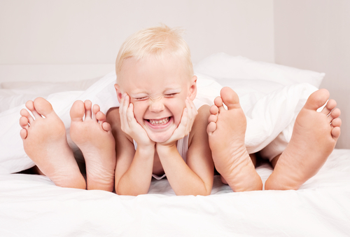 Smilende dreng ligger fodenden af sengen med hans forældres fødder, der stikker ud af dynen.