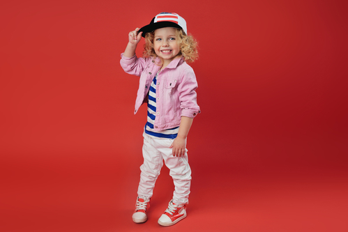 Smilende børnemodel (pige) med kasket foran rød baggrund