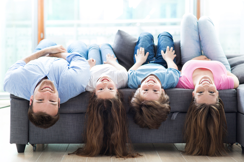 Familie med en mor, far og to børn ligger med hovedet ned af på en sofa.