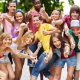 En stor gruppe glade, unge mennesker i sommerligt, farverigt tøj og med tommelfingeren opad.