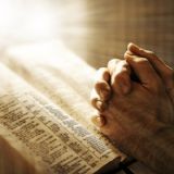 Bedende mandehænder på Biblen, mens en guddommeligt lys rammer Biblen