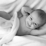 Sort/hid billed af baby, der smiler under et tæppe
