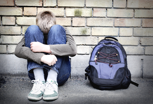 Dreng sidder sammenkrybende med skoletaske ved siden af sig.