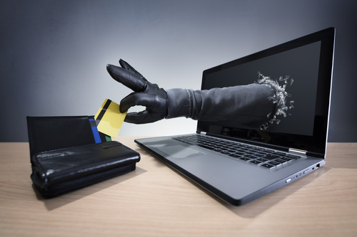 Handskeklædt hånd popper ud af en computerskærm og stjæler et kreditkort, der ligger på bordet ved siden af computeren.