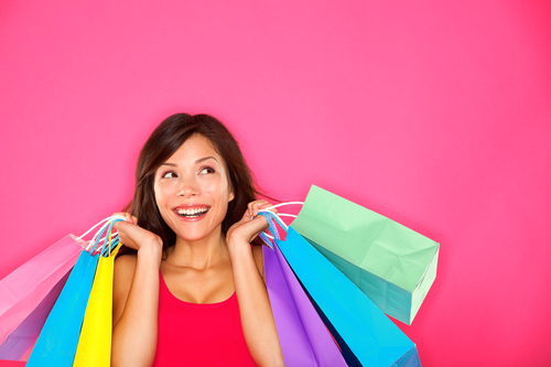 Smilende kvinde med farverige indkøbsposer foran lyserød baggrund