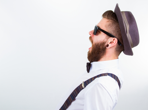 Hipster mand i profil med fuldskæg, hat, solbriller og seler.