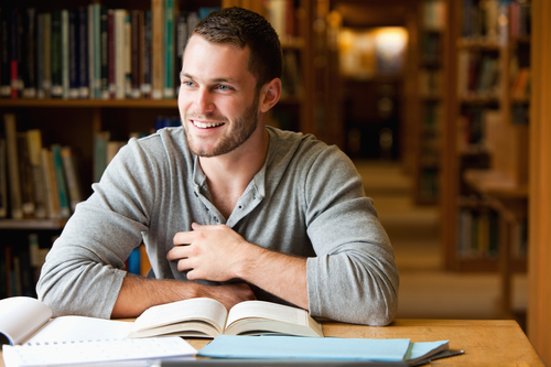 Mandlig studerende sidder på et bibliotek og læser