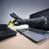Handskeklædt hånd popper ud af en computerskærm og stjæler et kreditkort, der ligger på bordet ved siden af computeren.