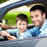 Søn sidder på skødet af far på førersædet i en bil