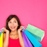 Smilende kvinde med farverige indkøbsposer foran lyserød baggrund