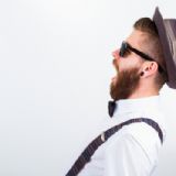 Hipster mand i profil med fuldskæg, hat, solbriller og seler.