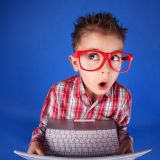 Fjollet ni-årig dreng med røde briller og computer.