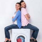 Mand og kvinde sidder smilende ovenpå en vaskemaskine med ryggen til hinanden