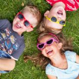 Billede af 3 små børn med solbriller på som ligger i græsset og griner